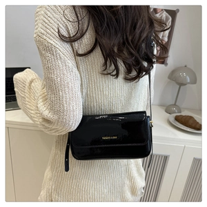 Detail of black patent leather crossbody bag with gold text and thin shoulder strap