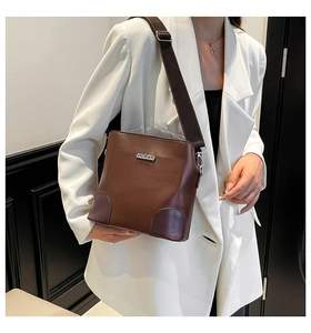 Detail of dark brown leather shoulder bag with metal logo and wide canvas strap on model