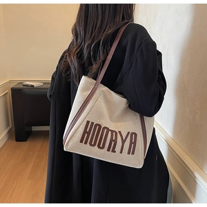 Detailed view of canvas tote bag with brown leather trim worn by model in black coat