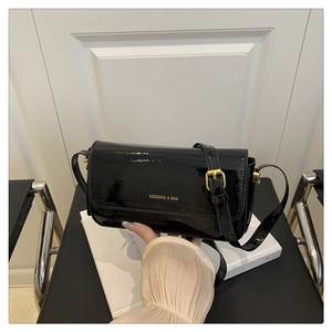 Detail of black patent leather crossbody bag with gold hardware and flap closure