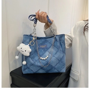 Detail of blue quilted denim tote bag with metal chain, pearl strap and cloud charm