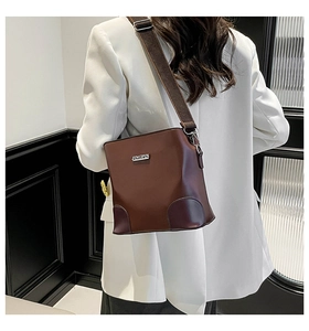 Close-up of brown PU leather bucket bag with silver metal logo and wide strap detail