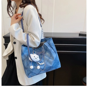 Detail of denim blue quilted tote bag with metal chain and white cloud charm