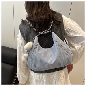 Detail of light blue textured crescent bag with silver zipper and white plush charm on model