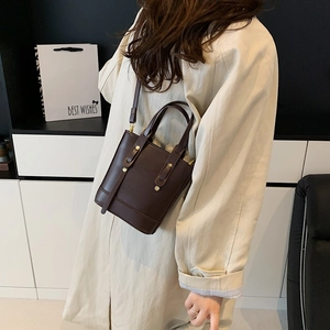 Sac seau en cuir marron foncé avec rivets dorés et bandoulière sur un trench-coat