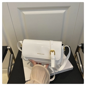 Close-up of white patent leather shoulder bag with golden buckle and brand logo detail