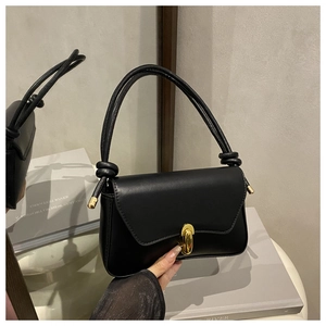 Detail of black leather handbag with a gold oval twist lock and a knotted handle design
