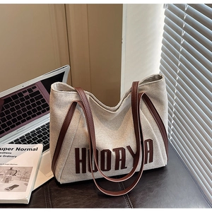 Detail of canvas tote bag with brown leather straps and large HUORYA letter print