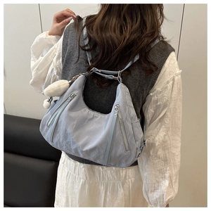 Detail of light blue nylon hobo bag with parallel zippers and a white plush keychain