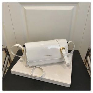 Close-up of white patent leather crossbody bag with adjustable buckle on a minimal setup