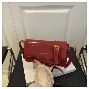Detail of burgundy patent leather handbag featuring glossy finish and gold logo accents