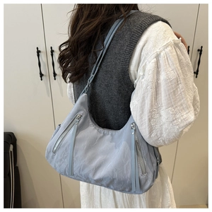 Close-up of light blue pleated nylon tote bag with silver zippers worn by a model