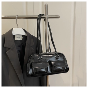 Detail of black patent leather baguette bag with dual front flap pockets on a metal hanger