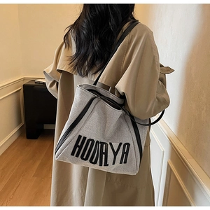 Detailed shoulder view of a grey canvas tote bag with black leather trim and HOORYA logo
