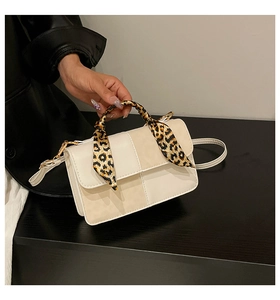 Detail of off-white crossbody bag featuring a leopard print scarf wrapped around the handle