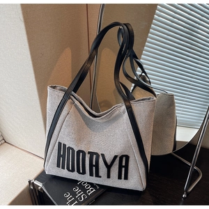 Detail of greyish-white canvas tote bag featuring black leather trim and bold HOORYA lettering