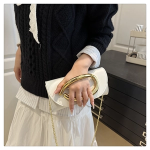 Detail of white leather handbag with oversized gold metal handle and chain strap