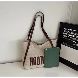 Detail of canvas tote bag with brown HOORY print and leather straps on a desk