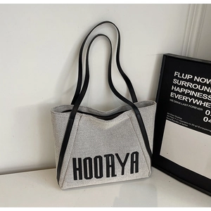 Detail of grey canvas tote bag with large black HOORYA text and slim black leather handles