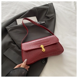 Detail of burgundy crocodile pattern handbag with gold clasp on a dark blazer