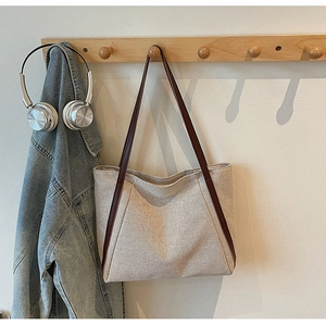 Detail of high-quality canvas tote bag with brown trim hanging on a wooden hook