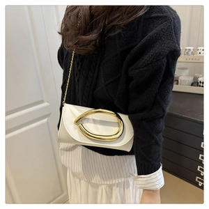 Detail of a white patent leather envelope bag with gold chain and large metal buckle