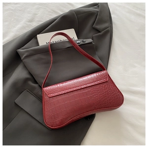 Detail of dark red baguette bag with glossy crocodile texture on grey suit