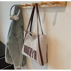 Close-up of canvas tote bag hanging on wooden hook with HOOAYA logo and leather straps