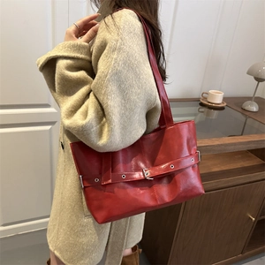 Glossy red faux leather tote bag with buckle details shown in a modern interior setting
