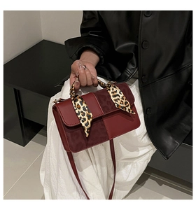 Detail of wine red crossbody bag featuring a leopard print scarf wrapped around the handle