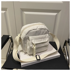 Detail of white corduroy crossbody bag featuring a front pocket and woven zipper pull