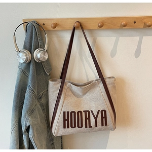 Detail of off-white canvas tote bag with HOORYA text and brown leather straps