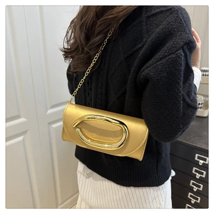 Detail of a metallic gold evening clutch bag with chain strap on a model's shoulder