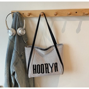 Detail of canvas tote bag with HOORYA text hanging on a wooden hook with headphones