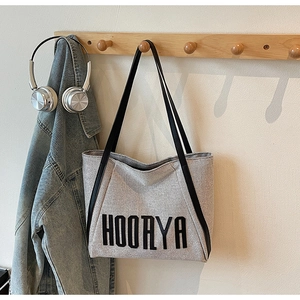 Close-up of canvas tote bag with HOORYA lettering and black leather shoulder straps