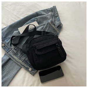 Detail of black corduroy crossbody bag with woven zipper pull on denim jacket