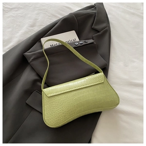 Close-up of light green baguette bag with crocodile pattern on grey suit background