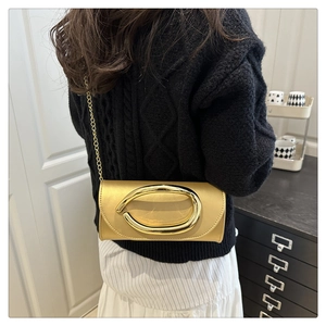 Detail of a chic golden chain bag with an oversized oval buckle worn over a black sweater