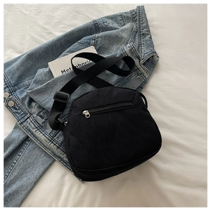 Close-up of black corduroy crossbody bag texture and rear zipper pocket on blue denim fabric