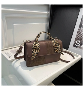 Detail of brown crossbody bag featuring leopard print accents and silk scarf handle