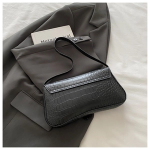 Detail of black crocodile pattern baguette shoulder bag on a grey textured suit blazer