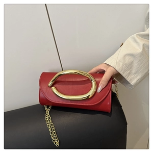 Detail of red leather evening clutch featuring a large gold round metal buckle and chain