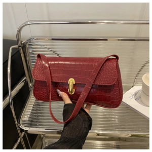 Detail of burgundy crocodile pattern baguette bag with a golden metal twist lock closure