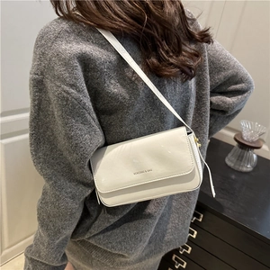 Chic white patent leather baguette shoulder bag shown on shoulder with knit sweater