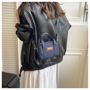 Rear view of a model wearing a mini denim crossbody bag with white stitching and leather patch