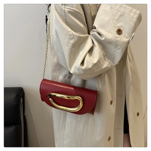 Detail of red leather chain bag featuring a large twisted gold metal accent and fine strap
