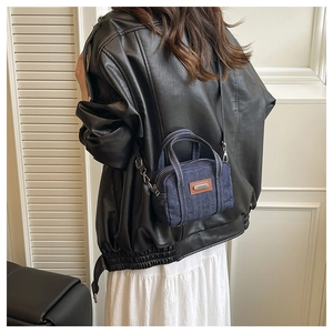 Detail of vintage navy denim crossbody bag with brown leather patch and metallic logo
