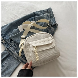 Detailed close-up of white corduroy crossbody bag with woven pendant and adjustable strap