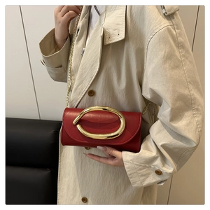Detail of red leather rectangular clutch bag featuring a prominent gold oval metal buckle