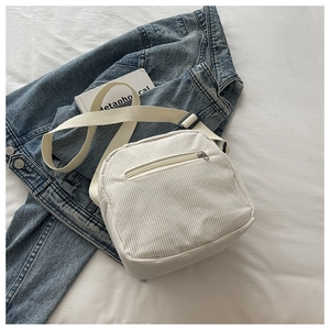 Detail view of white corduroy crossbody bag with adjustable strap on denim jacket